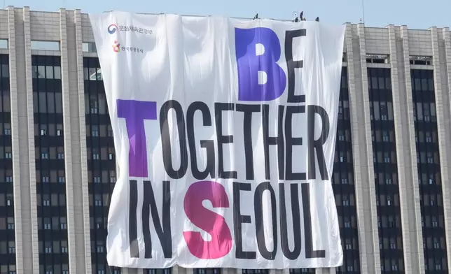 Workers adjust a banner promoting a comeback concert of K-pop boy group BTS on the government complex building near Gwanghwamun Square in Seoul, South Korea, Friday, March 20, 2026. (AP Photo/Ahn Young-joon)
