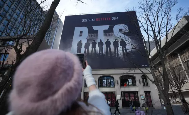 A fan of K-pop band BTS films billboard showing of BTS in downtown Seoul, South Korea, Thursday, March 19, 2026. (AP Photo/Lee Jin-man)