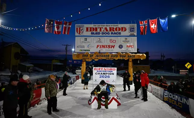 Jessie Holmes poses with his lead dogs Zeus, left, and Polar, after claiming his second straight Iditarod Trail Sled Dog Race championship, in Nome, Alaska, Tuesday March 17, 2026. (Marc Lester/Anchorage Daily News via AP)