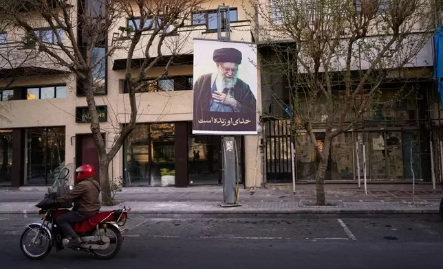 A motorcycle drives past a picture of the late Iranian Supreme Leader Ayatollah Ali Khamenei along an empty street in Tehran, Iran, Sunday, March 1, 2026, following the confirmed death of Khamenei in U.S. and Israeli strikes. (AP Photo/Vahid Salemi)