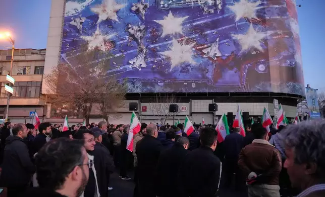 Government supporters gather in mourning after state TV officially announced the death of Iranian Supreme Leader Ayatollah Ali Khamenei, under a billboard with graphic showing a U.S aircraft carrier with damaged fighter jets on its deck, in Tehran, Iran, Sunday, March 1, 2026. (AP Photo/Vahid Salemi)