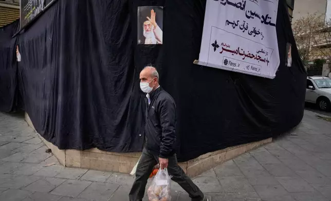 AA man carrying groceries walks by a picture of the late Iranian Supreme Leader Ayatollah Ali Khamenei hanging on a black sheet along the side of a mosque in Tehran, Iran, Monday, March 2, 2026. (AP Photo/Vahid Salemi)
