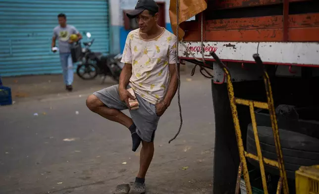 A vendor holds a wad of Bolivar bills at market in Caracas, Venezuela, Wednesday, March 11, 2026. (AP Photo/Ariana Cubillos)