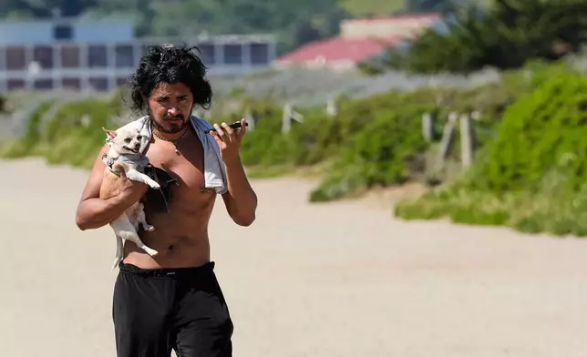 Enrique Martinez carries his 11-year-old dog Pepe so it doesn't have to walk on the hot sand at Crissy Field in San Francisco, Tuesday, March 17, 2026. (AP Photo/Godofredo A. Vásquez)