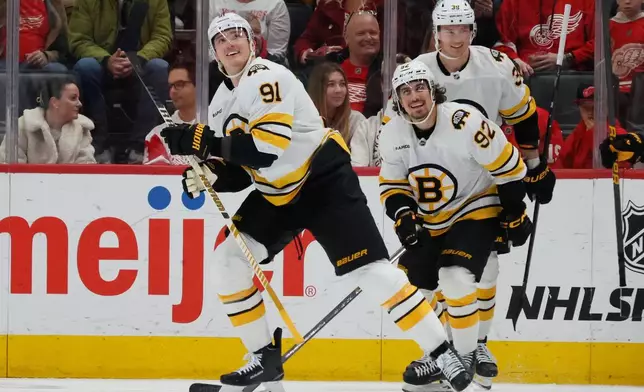 Boston Bruins defenseman Nikita Zadorov (91) smiles with teammates center Marat Khusnutdinov (92) and center Morgan Geekie (39) after scoring a goal against the Detroit Red Wings during the third period of an NHL hockey game Saturday, March 21, 2026, in Detroit. (AP Photo/Duane Burleson)