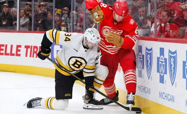 Boston Bruins left wing Tanner Jeannot (84) tries to dig the puck out from under Detroit Red Wings defenseman Ben Chiarot (8) during the second period of an NHL hockey game Saturday, March 21, 2026, in Detroit. (AP Photo/Duane Burleson)