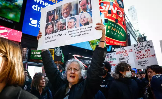 A woman holds up a placard with images of President Donald Trump and some of his cabinet members, during a protest against U.S. and Israeli strikes on Iran, in New York, Saturday, Feb. 28, 2026. (AP Photo/Kena Betancur)