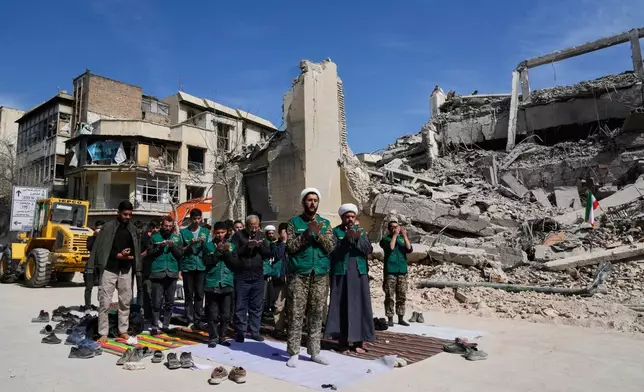 A cleric leads a group of volunteers in prayer next to a police facility struck during the U.S.–Israeli military campaign in Tehran, Iran, Wednesday, March 4, 2026. (AP Photo/Vahid Salemi)