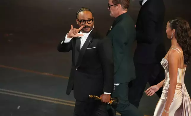 Robert Downey Jr., right, walks alongside Ryan Coogler after Coogler won the award for writing (original screenplay) for "Sinners" during the Oscars on Sunday, March 15, 2026, at the Dolby Theatre in Los Angeles. (AP Photo/Chris Pizzello)