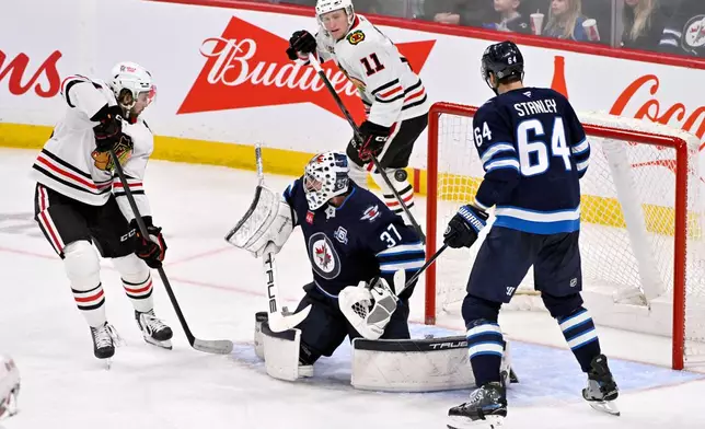 A shot deflected by Chicago Blackhawks' Landon Slaggert (left) goes over Winnipeg Jets goaltender Connor Hellebuyck (37) during the third period of their NHL hockey game in Winnipeg, Tuesday March 3, 2026. (Fred Greenslade/The Canadian Press via AP)