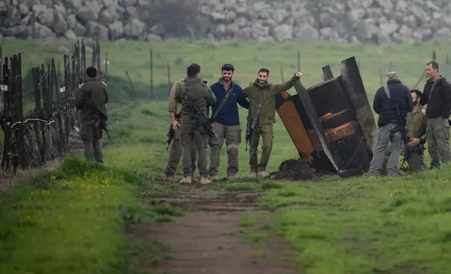 Israeli soldiers take photographs next to a fragment of a missile fired from Iran, and intercepted by Israeli defense system, embedded in an open field in the Israeli-controlled Golan Heights, Thursday, March 19, 2026. (AP Photo/Ohad Zwigenberg)