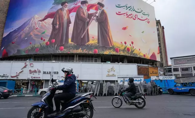 Motorbikes drive past a billboard depicting Iran’s late Supreme Leader Ayatollah Ali Khamenei, center, handing the country’s flag to his son and successor Ayatollah Mojtaba Khamenei, right, as the late revolutionary founder Ayatollah Ruhollah Khomeini stands at left, in a square in downtown Tehran, Iran, Tuesday, March 10, 2026. (AP Photo/Vahid Salemi)
