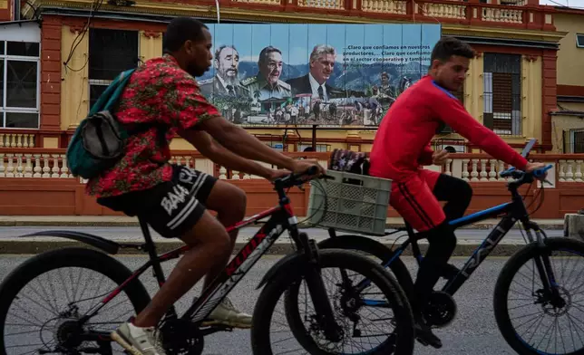 People ride their bicycles in front of images of, from left, past presidents Fidel Castro and Raul Castro, and current President Miguel Diaz-Canel, in Havana, Wednesday, March 18, 2026. (AP Photo/Ramon Espinosa)