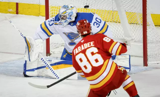 St. Louis Blues goalie Joel Hofer, left, lets in a goal from Calgary Flames' Joel Farabee that was later called back during second period NHL hockey action in Calgary on Wednesday, March 18, 2026. (Jeff McIntosh/The Canadian Press via AP)