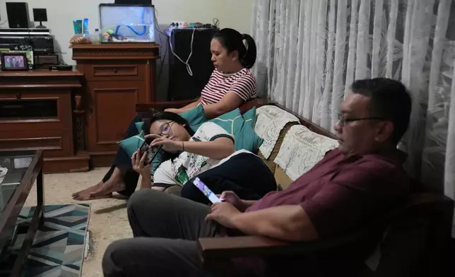 Maura Munthe, center, and her parents Lena Sinuraya, rear, and Ronald, right, use their mobile phone at their house in Jakarta, Indonesia, March 14, 2026. (AP Photo/Dita Alangkara)