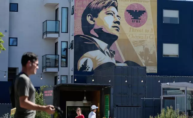 Pedestrians walk below an image of César Chavez on a mural in San Francisco, Wednesday, March 18, 2026. (AP Photo/Jeff Chiu)