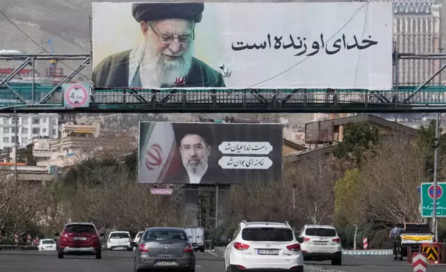 Vehicles drive under billboards showing portraits of the late Iranian Supreme Leader Ayatollah Ali Khamenei, foreground, and his son Ayatollah Mojtaba Khamenei, the successor to him, along a highway in Tehran, Iran, Tuesday, March 24, 2026. (AP Photo/Vahid Salemi)