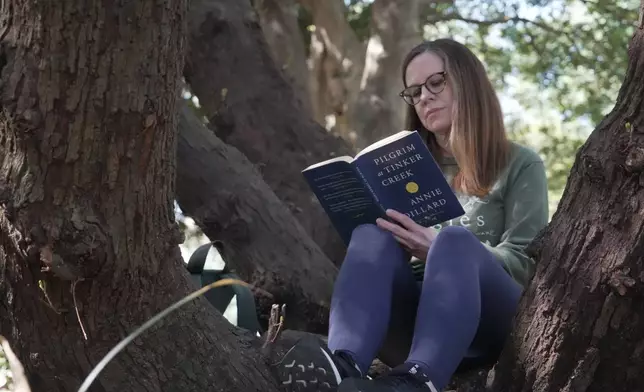 Claire Jefferies reads a book in the crotch of an oak tree during a "forest bathing" session at the J.C. Raulston Arboretum in Raleigh, N.C., on Sunday, March 22, 2026. (AP Photo/Allen G. Breed)