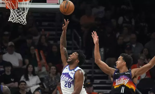 Utah Jazz forward Brice Sensabaugh (28) gets off a shot against Phoenix Suns forward Oso Ighodaro (11) during the first half of an NBA basketball game, Saturday, March 28, 2026, in Phoenix. (AP Photo/Ross D. Franklin)