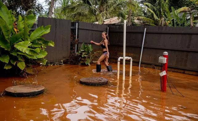 Linda Griffith wades through a flooded yard in Haleiwa, Hawaii Saturday, March 21, 2026. (Stephen Lam/San Francisco Chronicle via AP)