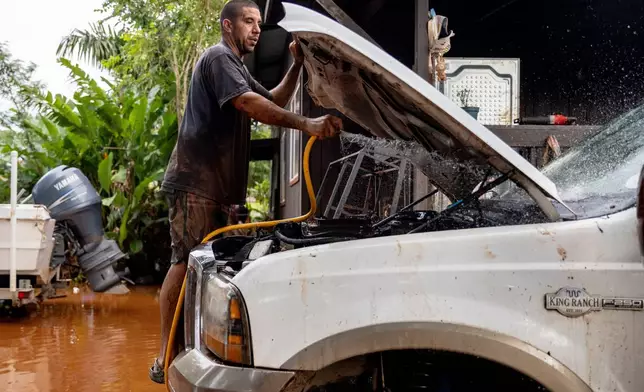 Philip Holman flushes mud from his lifted truck's engine bay the day after it was fully submerged by the fast-moving flood in Haleiwa, Hawaii Saturday, March 21, 2026. (Stephen Lam/San Francisco Chronicle via AP)