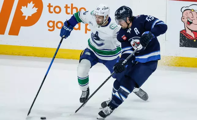 Winnipeg Jets' Mark Scheifele (55) and Vancouver Canucks' Max Sasson (63) battle for the puck during first-period NHL hockey game action in Winnipeg, Manitoba, Saturday, March 7, 2026. (John Woods/The Canadian Press via AP)