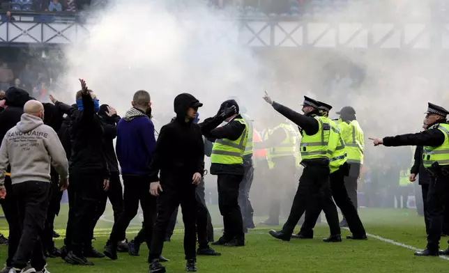 Police officer and stewards force fans back after they invaded the pitch following a penalty shoot out after the Scottish Cup quarterfinal soccer match between Rangers and Celtic, in Glasgow, Scotland, Sunday March 8, 2026. (Steve Welsh/PA via AP)