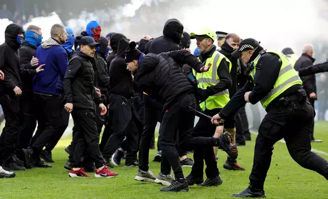 Police officer and stewards force fans back after they invaded the pitch following a penalty shoot out after the Scottish Cup quarterfinal soccer match between Rangers and Celtic, in Glasgow, Scotland, Sunday March 8, 2026. (Steve Welsh/PA via AP)