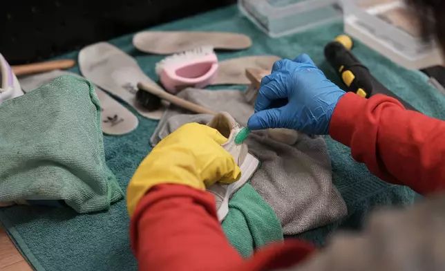 A worker uses a toothbrush to clean a used sneaker at SneakCoeurZ, a nonprofit organization giving used footwear a second life, in Champs-sur-Marne, east of Paris, Wednesday, March 25, 2026. (AP Photo/Thibault Camus)