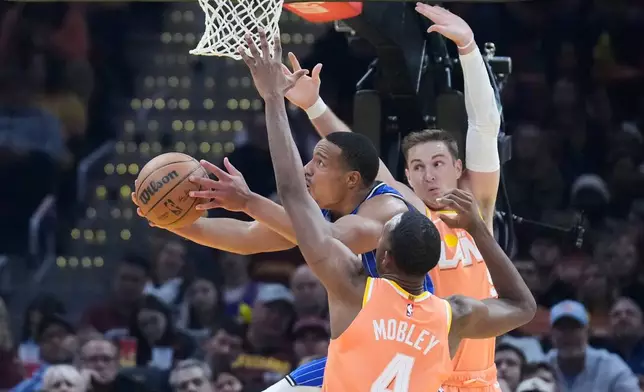 Orlando Magic guard Desmond Bane, left, goes to the basket between Cleveland Cavaliers center Evan Mobley (4) and guard Sam Merrill, right, in the first half of an NBA basketball game in Cleveland, Tuesday, March 24, 2026. (AP Photo/Sue Ogrocki)