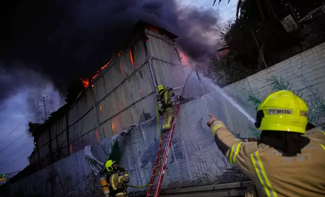 Firefighters try to extinguish flames at the site of a direct hit by an Iranian missile strike in Holon, central Israel, Friday, March 13, 2026. (AP Photo/Ohad Zwigenberg)
