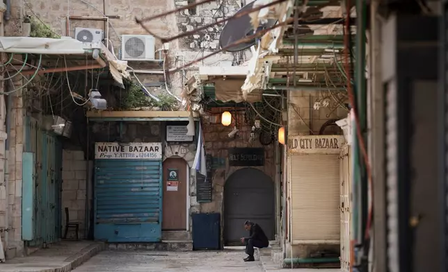 A man sits beside a locked door of the Church of the Holy Sepulchre and shuttered shops in Jerusalem’s Old City, which remains off limits to visitors amid the war with Iran, Friday, March 27, 2026. (AP Photo/Mahmoud Illean)