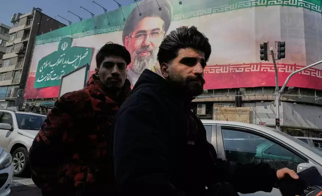 Two men ride their motorbike past a billboard of the Iranian Supreme Leader Ayatollah Mojtaba Khamenei in downtown Tehran, Iran, Saturday, March 14, 2026. (AP Photo/Vahid Salemi)