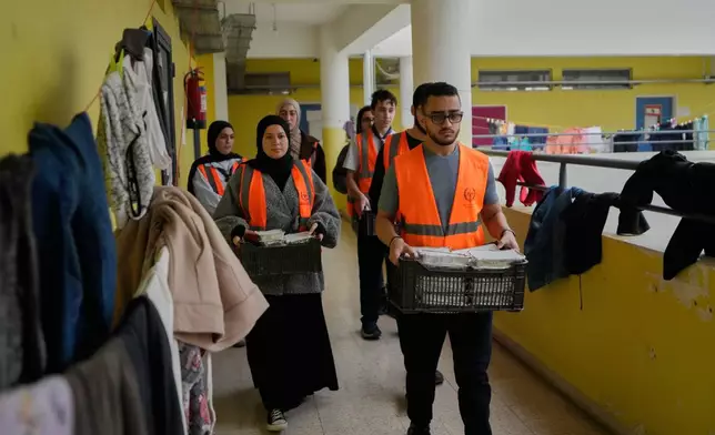 Volunteers carrying meals to be distributed for displaced people who fled Israeli strikes from south Lebanon at a school turned into a shelter, in the southern port city of Sidon, Lebanon, Saturday, March 14, 2026. (AP Photo/Mohammed Zaatari)