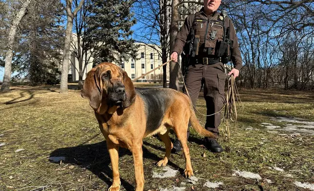 North Dakota Highway Patrol Trooper Steven Mayer and Bleu, a bloodhound, stand for a photo, Feb. 11, 2026, near the state Capitol in Bismarck, N.D. (AP Photo/Jack Dura)