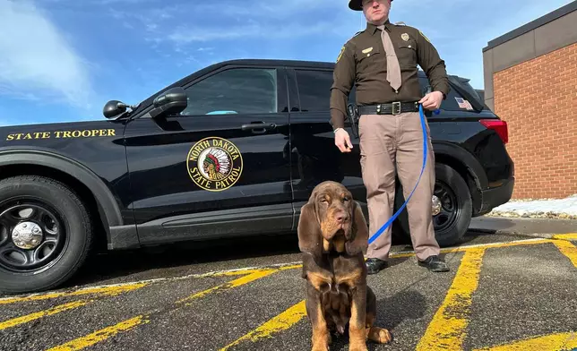 North Dakota Highway Patrol Trooper Dustin Pattengale and Beau, a bloodhound puppy, pose for a photo on Friday, Feb. 27, 2026, outside the Highway Patrol office in Fargo, N.D. (AP Photo/Jack Dura)
