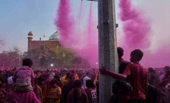 Children watch as revelers dance under colored water and powder sprayed from above at the Shri Krishna Janmabhoomi Temple complex during Holi festival celebrations in Mathura, India, on Feb. 27, 2026. (AP Photo/Manish Swarup)