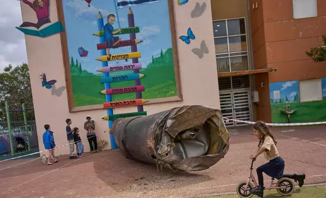 Children play beside a fragment of an Iranian ballistic missile that landed in a schoolyard in the Israeli settlement of Peduel in the West Bank Monday, March 23, 2026. (AP Photo/Ohad Zwigenberg)