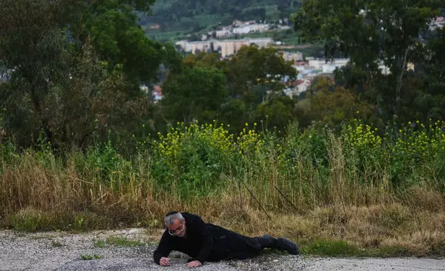 A man takes cover as air raid sirens sound, warning of rockets launched from Lebanon toward Israel, in Kiryat Shmona, northern Israel, Monday, March 23, 2026. (AP Photo/Ariel Schalit)