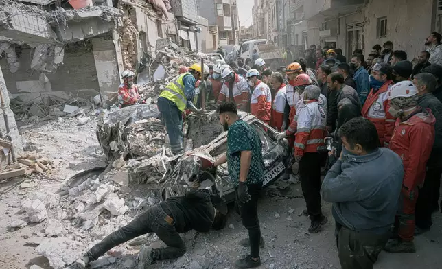First responders inspect a destroyed car at the site of a residential building hit in an overnight strike during the U.S.-Israeli military campaign in Tabriz, East Azerbaijan Province, northwestern Iran, Tuesday, March 24, 2026. (AP Photo/Matin Hashemi)