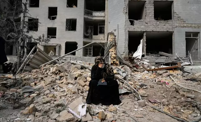 A woman sits on rubble across from a residential building damaged last Monday during the U.S.-Israeli air campaign in Tehran, Iran, Thursday, March 12, 2026. (AP Photo/Vahid Salemi)