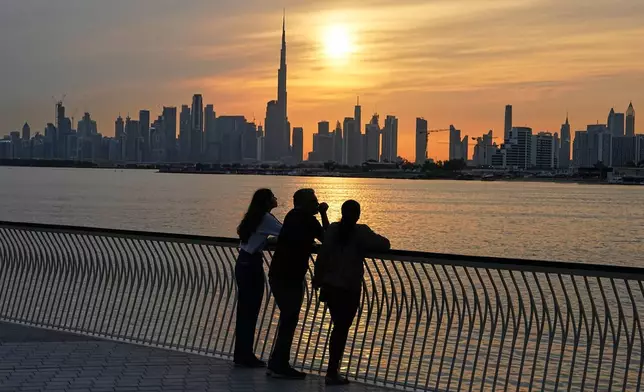 A family enjoys the sunset with the view of the city skyline and Burj Khalifa, at Dubai Creek Harbour in Dubai, United Arab Emirates, Wednesday, March 11, 2026. (AP Photo/Fatima Shbair)