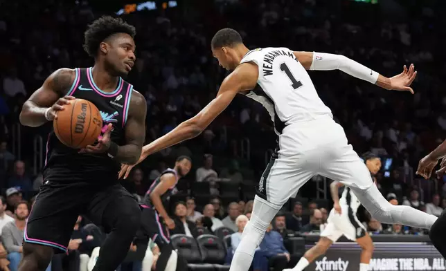 Miami Heat's Davion Mitchell, left, grabs a rebound over San Antonio Spurs forward Victor Wembanyama (1) during the first half of an NBA basketball game, Monday, March 23, 2026, in Miami. (AP Photo/Lynne Sladky)