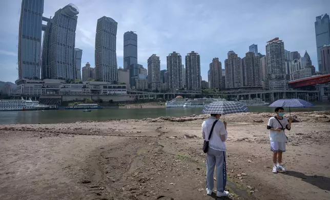 FILE - Students carrying umbrellas stand on the dry riverbed of the Jialing Rivera, a tributary of the Yangtze, in southwestern China's Chongqing Municipality, Aug. 19, 2022. (AP Photo/Mark Schiefelbein, File)