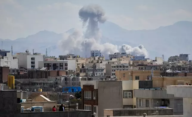 People watches from rooftop as a plume of smoke rises after a strike in Tehran, Iran, Sunday, March 1, 2026. (AP Photo/Vahid Salemi)
