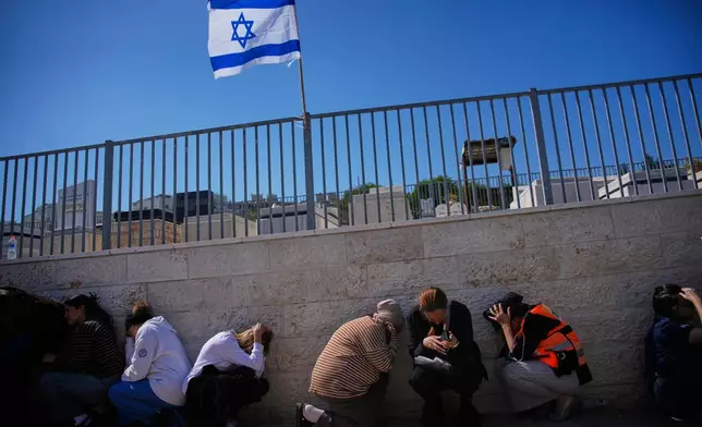 Mourners take cover while air-raid sirens warn of incoming missiles launched by Iran toward Israel during the funeral of Sarah Elimelech and her daughter Ronit who were killed in an Iranian missile attack, in Beit Shemesh, Israel, Monday, March 2, 2026. (AP Photo/Ohad Zwigenberg)