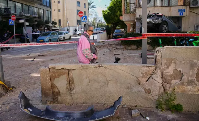 A woman walks past a cordoned-off area damaged during an Iranian strike in Tel Aviv, Israel, Sunday, March 8, 2026. (AP Photo/Ohad Zwigenberg)
