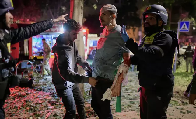 Rescue workers bandage a wounded man and provide first aid at the site of a direct hit from an Iranian missile strike in Tel Aviv, Israel, Saturday, Feb. 28, 2026. (AP Photo/Tomer Neuberg)