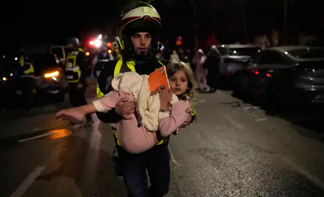 An Israeli rescue personal carries a child after missiles attack from Iran hit in Tel Aviv, Israel, Saturday, Feb. 28, 2026. (AP Photo/Ohad Zwigenberg)