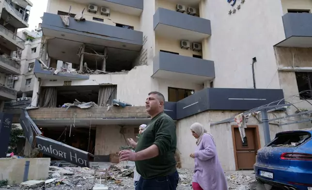 People pass in front of a damaged hotel that was hit by an Israeli airstrike in Hazmieh east of Beirut, Lebanon, Wednesday, March 4, 2026. (AP Photo/Hussein Malla)